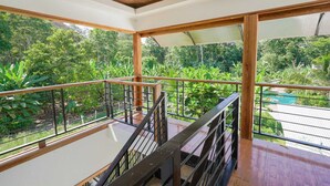 Balcón con piso de madera y baranda de metal, que da a un jardín verde y exuberante.