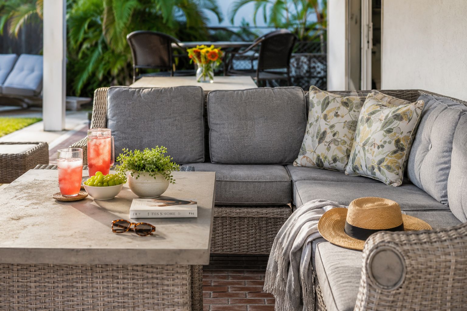 Un espace extérieur accueillant avec une table en osier, des coussins, une plante en pot et un livre.