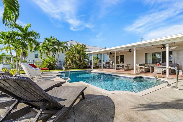 Une piscine avec des chaises longues, un patio couvert et des palmiers.