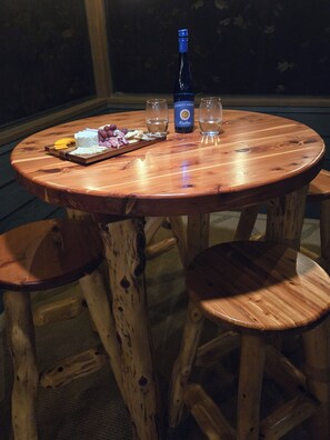 Une table ronde en bois, avec une bouteille de vin, deux verres et une planche à fromages garnie de différents fromages et de raisins.