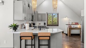 Una cocina moderna con una isla grande, dos taburetes de bar, luces colgantes y vistas al exterior.