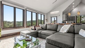 Una sala de estar moderna con un sofá modular, una mesa de centro de vidrio y grandes ventanales con vistas a zonas verdes.