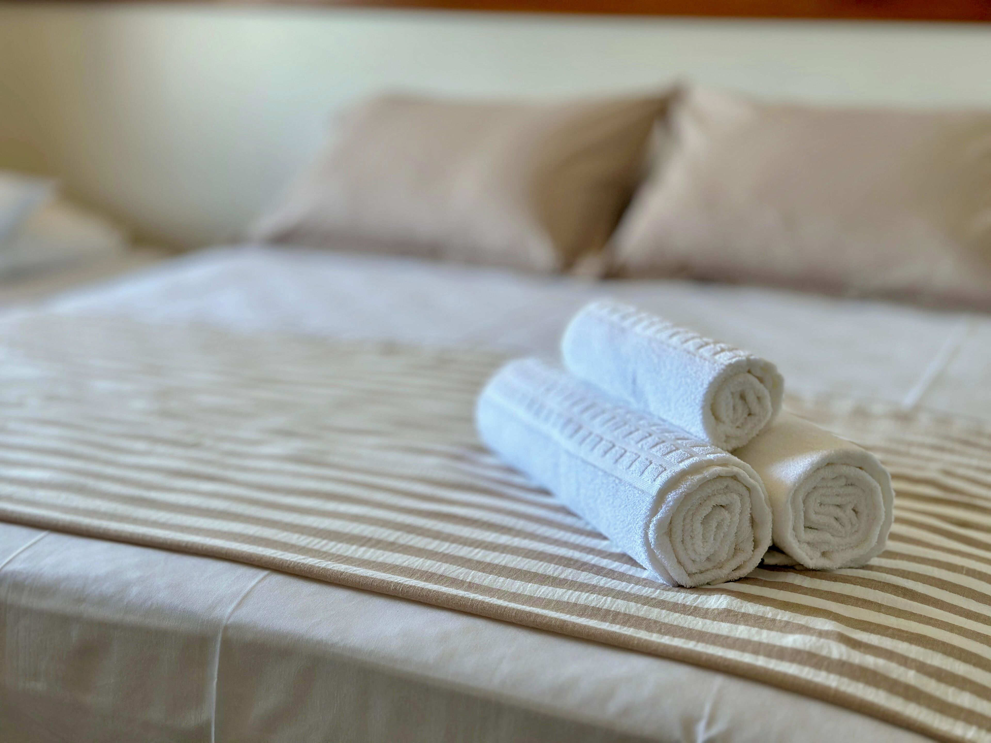 Cama bem arrumada com roupa de cama listrada e toalhas brancas dobradas.