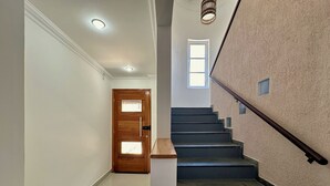 Una scala con una porta in legno in cima, un lampadario sopra e una pianta sullo sfondo.