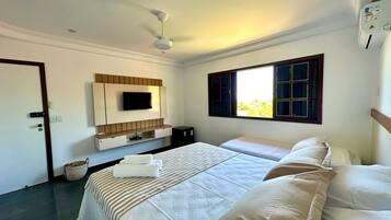 Quarto de hotel com duas camas, televisão na parede, ventoinha no teto e janela com vista para o verde lá fora.