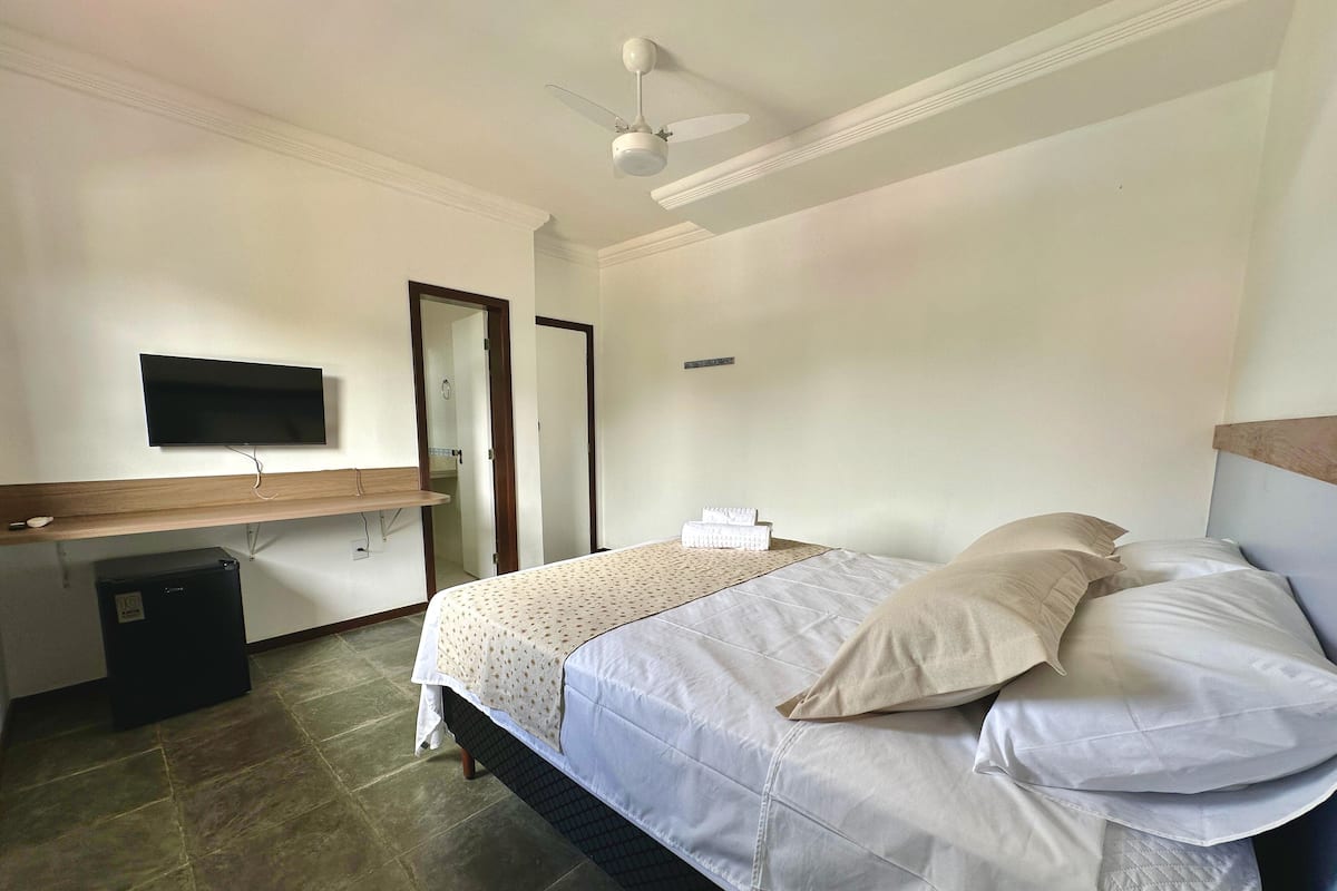 A bedroom with a bed, a desk, a television, and a ceiling fan.