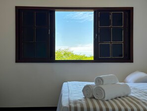A room with a bed, two rolled towels, and a window with a view of greenery and the sky. - Pousada Mar de Corais (Serra)