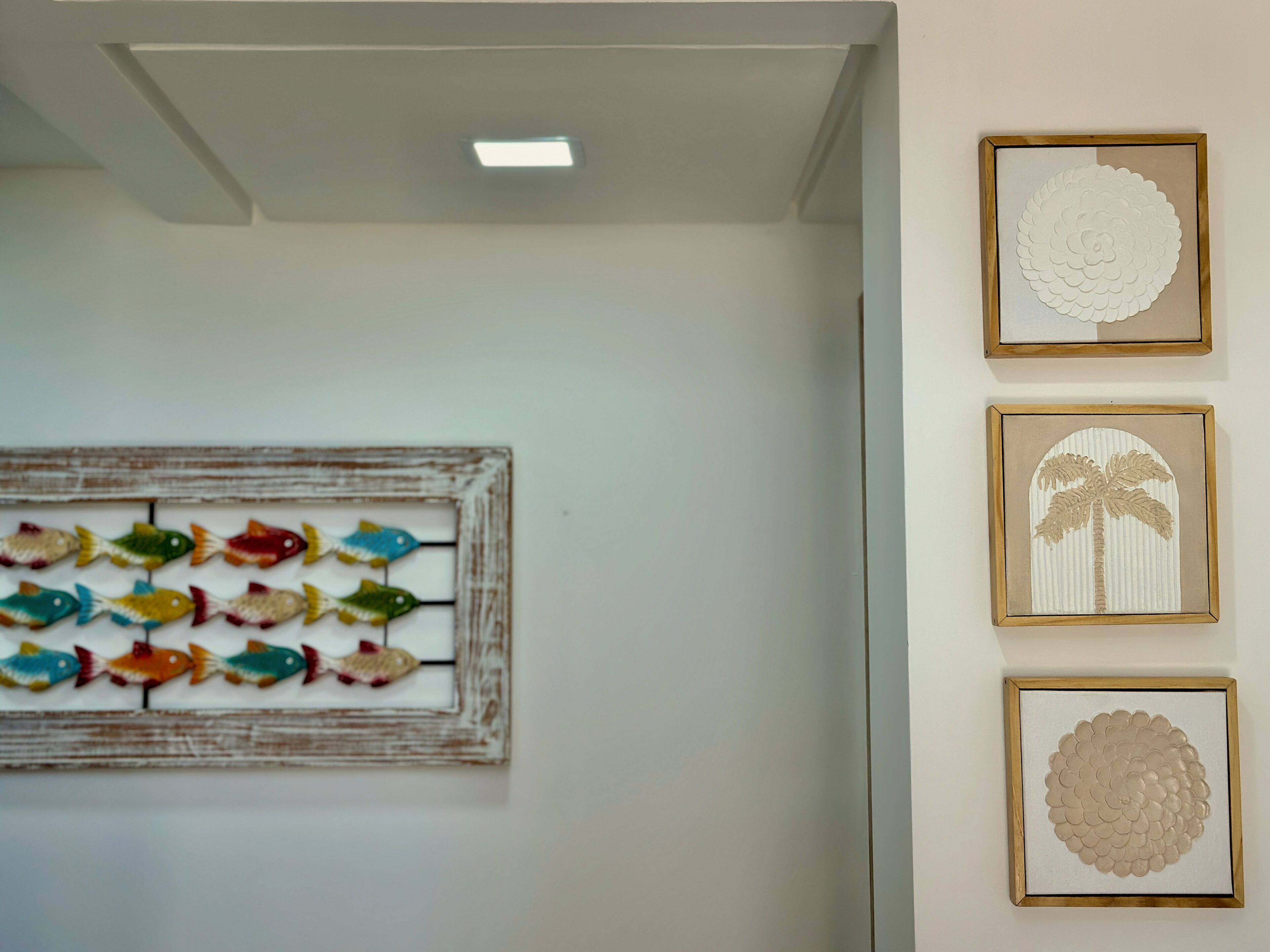 Paredes com três quadros: um mural colorido de peixes, uma palmeira e um design circular.