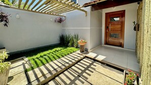Un cortile con una pergola in legno, un patio con piastrelle e una porta con cornice in legno.