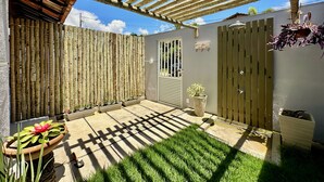Un patio coperto con una pergola in legno, un piccolo giardino con piante in vaso e un pavimento in cemento.