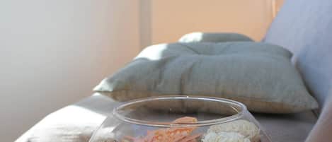 A clear glass bowl with dried flowers and nuts on a table in a room with a bed and a window.