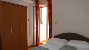 Une chambre à coucher comprenant un lit, des oreillers, une armoire et une porte-fenêtre coulissante donnant sur un balcon.