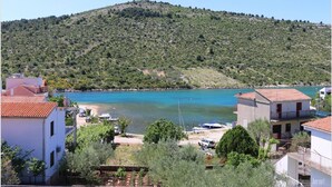 Une vue côtière avec une colline, une eau d’un bleu limpide et des bâtiments aux toits recouverts de tuiles rouges.