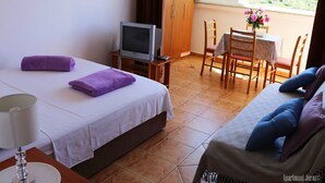 A hotel room with a bed, a TV, a dining table with chairs, and a view of the outdoors. - Apartments Juras - Studio Apartment with Sea View (Mia) (Rogoznica)