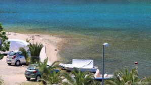 A beach with clear blue water, a sandy shore, parked cars, and a boat. - Apartments Juras - Studio Apartment with Sea View (Mia) (Rogoznica)