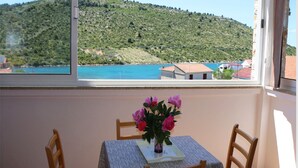 A room with a table and chairs, a window with a view of a hillside and a body of water. - Apartments Juras - Studio Apartment with Sea View (Mia) (Rogoznica)
