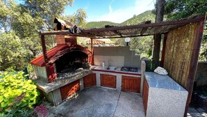 Eine Außenküche mit Backofen, Spüle und Gasherd, umgeben von einer Pergola und üppiger Bepflanzung.