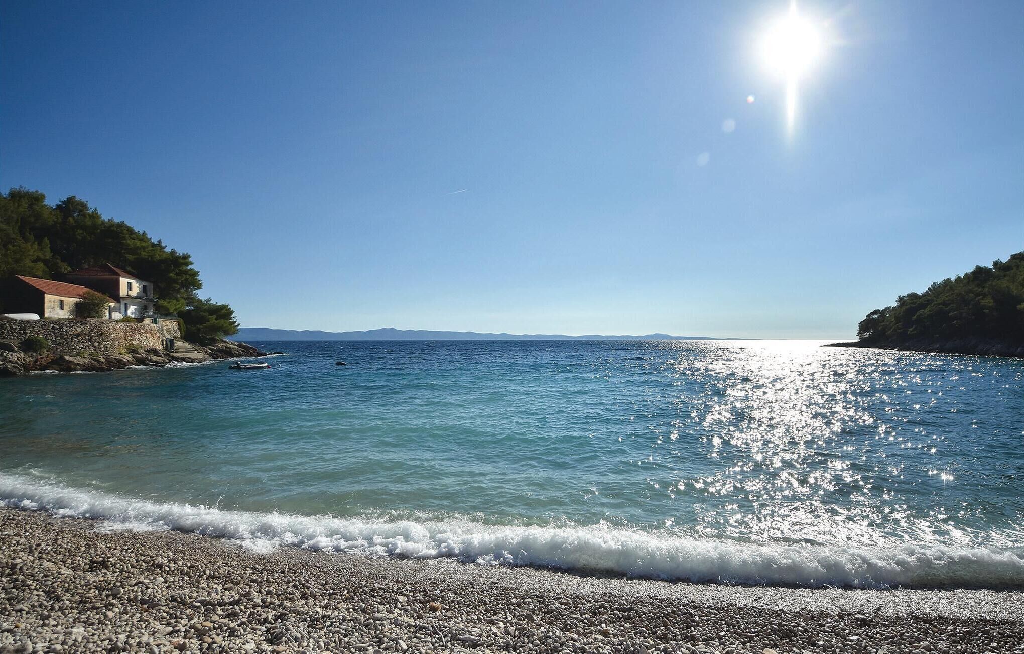 Kustgezicht met een kiezelstrand, heldere blauwe zee en een huis op een rotsachtige klif.