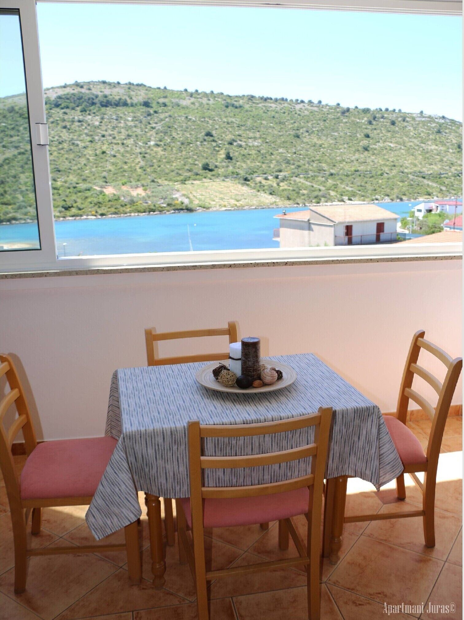 Un comedor con mesa y sillas, vistas a una ladera y al agua, y una ventana.