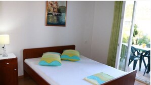 Quarto com cama de madeira, duas almofadas, mesa de cabeceira, luminária e um quadro na parede.