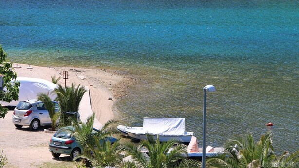 A beach with clear blue water, a sandy shore, parked cars, and a boat. - Apartments Juras - Studio Apartment with Loggia (Ana) (Rogoznica)