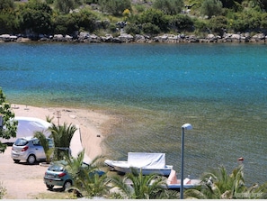 Een strand met helderblauw water, een zandstrand, geparkeerde auto's en een boot.