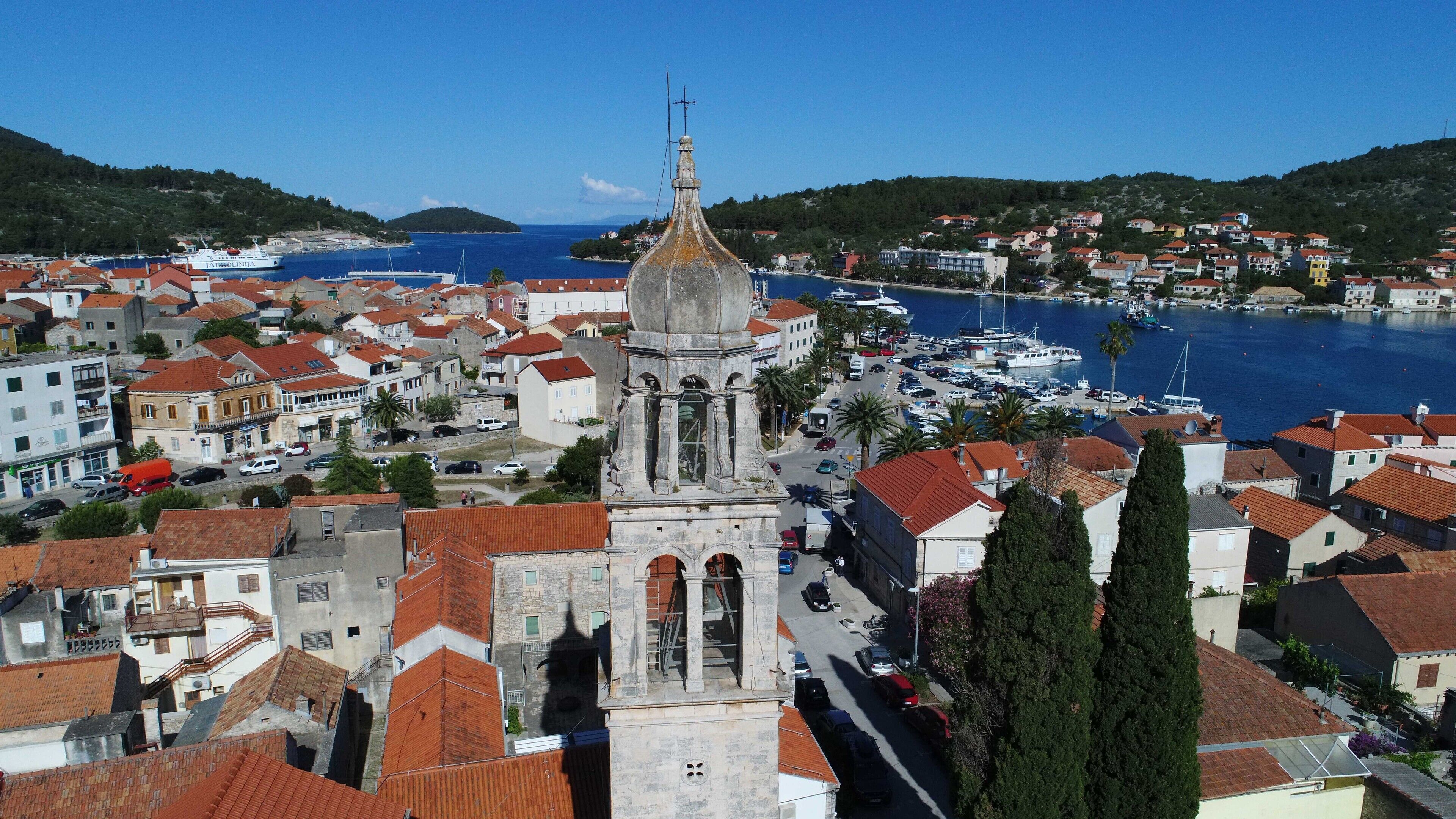 Un pueblo costero con una imponente torre de iglesia, un puerto deportivo con barcos y edificios de tejados rojos.