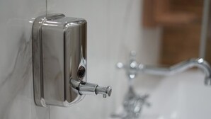 Un baño moderno con dispensador de jabón de pared y lavamanos visible.