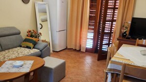A living room with a sofa, a coffee table, a dining table with chairs, a refrigerator, and a television. - Apartments Nada - Two Bedroom Apartment (A2) (Fazana)