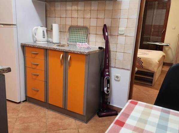 A compact kitchen with orange cabinets, a white kettle, a checkered cloth, and a vacuum cleaner. - Apartments Nada - One Bedroom Apartment (A4) (Fazana)