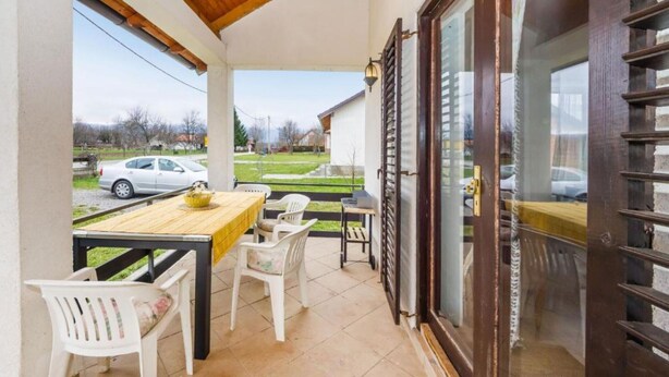 Un porche techado con mesa y sillas, techo de madera y vista a la calle y casas.