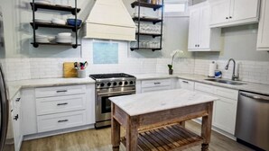 A modern kitchen with white cabinets, a stainless steel stove, wooden shelves, and hanging pendant lights. - Beautiful upstairs apartment for rent monthly near Audubon park (New Orleans)