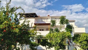A two-story house with a balcony, surrounded by greenery and a clear sky. - Apartments Verović Rab Banjol - One Bedroom Apartment With Terrace (A4) (Banjol)