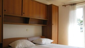 A single bed with a wooden headboard and two pillows, a window with a curtain, and a wooden wardrobe. - Apartments Verović Rab Banjol - One Bedroom Apartment With Terrace (A4) (Banjol)