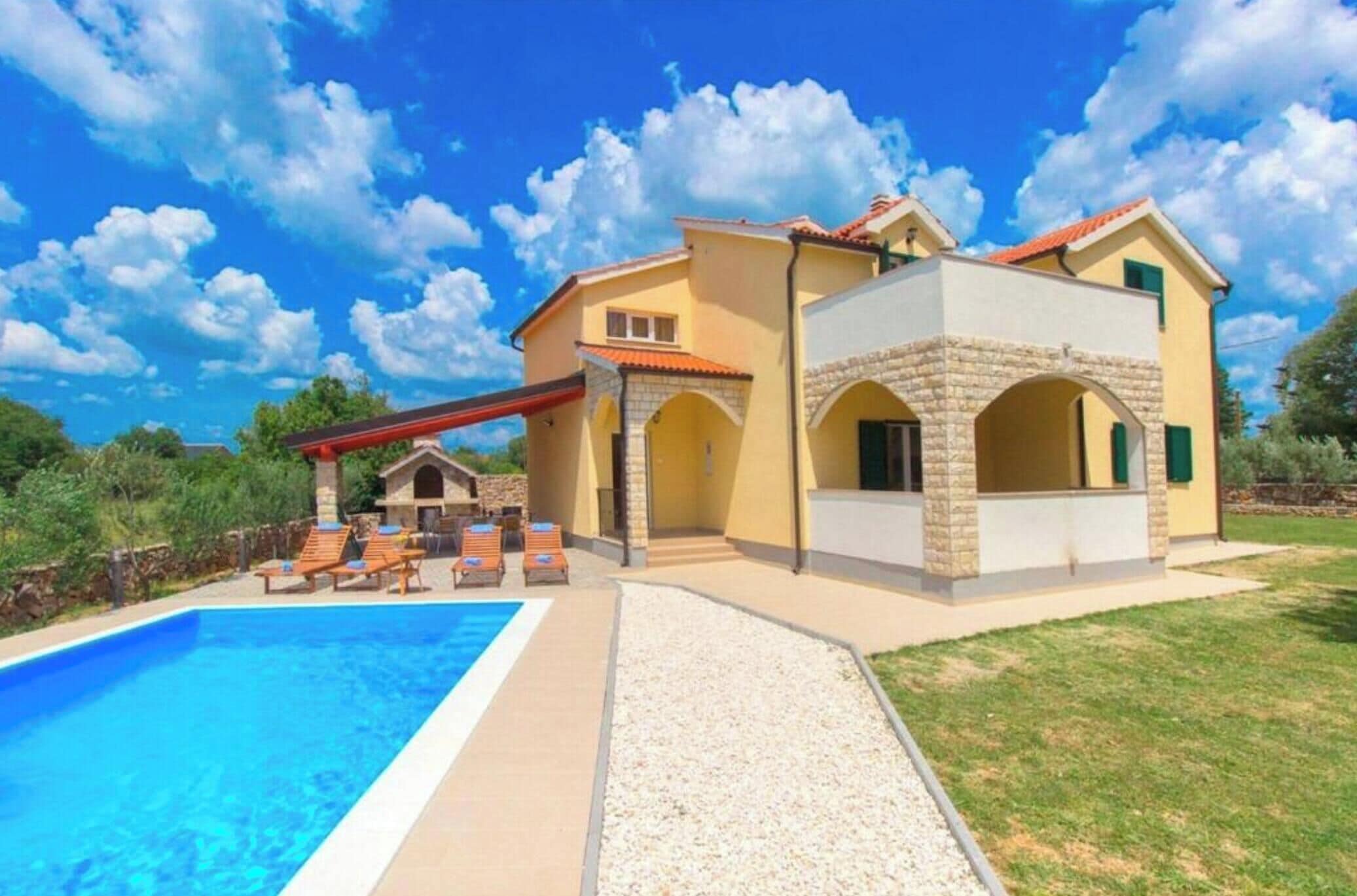 A two-story house with a swimming pool, outdoor seating, and a stone archway.