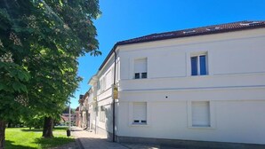 Ein weißes Gebäude mit einem Ziegeldach, einem gepflasterten Gehweg und einer begrünte Fläche mit Bäumen.