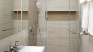 A modern bathroom with a glass shower enclosure, a sink, and a towel hanging on the wall.