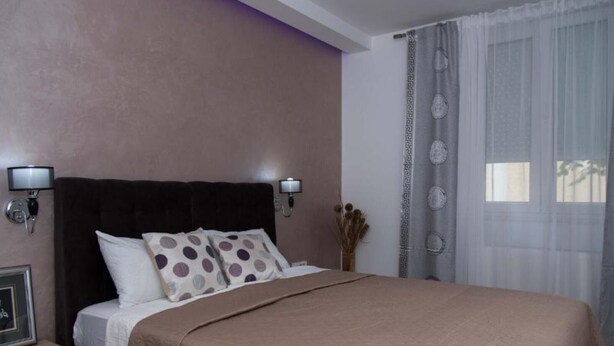 A neatly arranged bedroom with a large bed, two wall-mounted lamps, a bedside table, and a window with curtains.