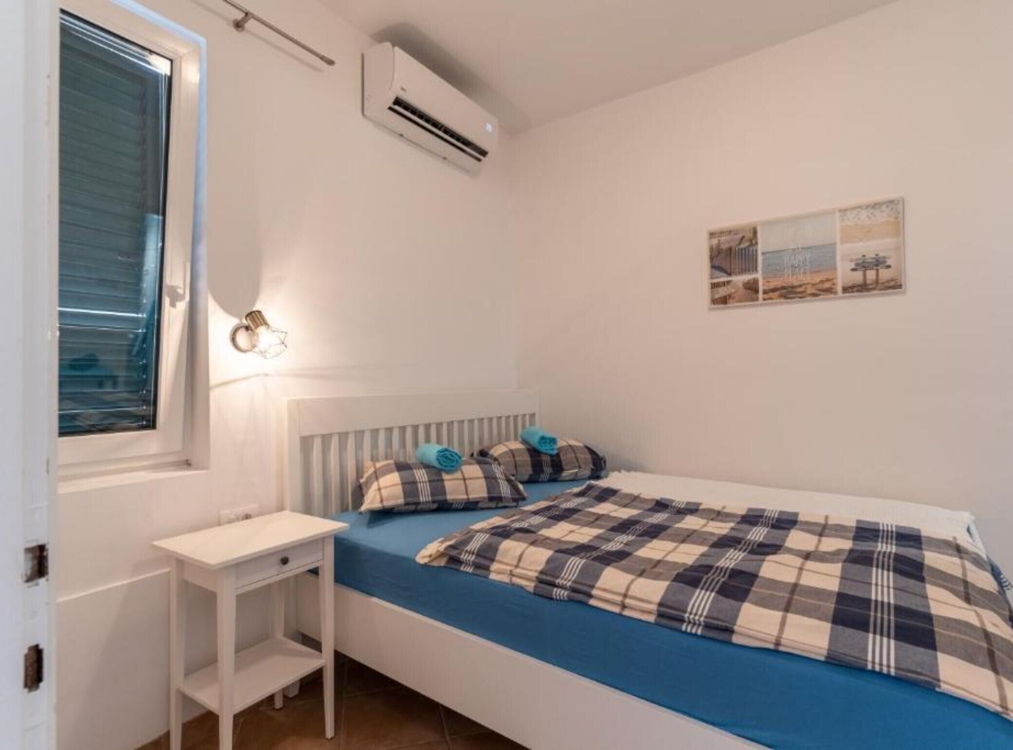 Quarto com cama, mesa de cabeceira, ar condicionado, janela e luminária na parede.