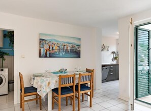 Ein Essbereich mit einem Tisch für vier Personen, einem Gemälde einer Küstenlandschaft und Blick in eine Küche.