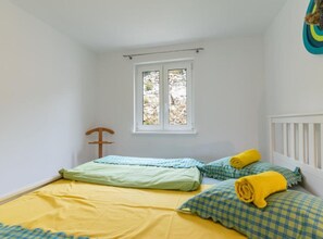 Ein kleiner, heller Raum mit einem Bett, einem Fenster und einem Holzsessel.