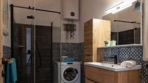 Un bagno funzionale con box doccia in vetro, lavatrice e mobile bagno in legno con specchio.