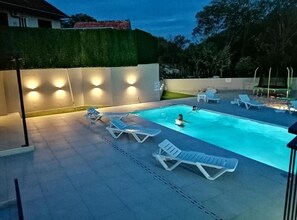A swimming pool with lounge chairs and a well-lit area. - (Vrgorac)