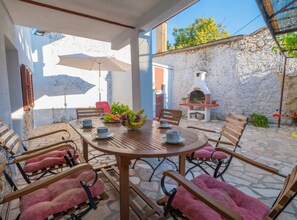 An outdoor patio with a round wooden table, chairs, and a fruit bowl. - Exquisite Holiday Home with Private Pool and Sauna - Three Bedroom Holiday Home (Tribalj)