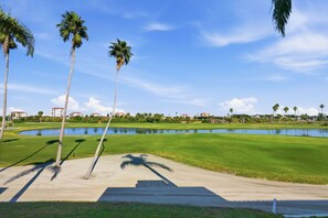 Ein Golfplatz mit Teich, Palmen und Gebäuden im Hintergrund.