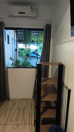 Een kamer met een raam, een houten vloer, een metalen ladder en een airconditioning.