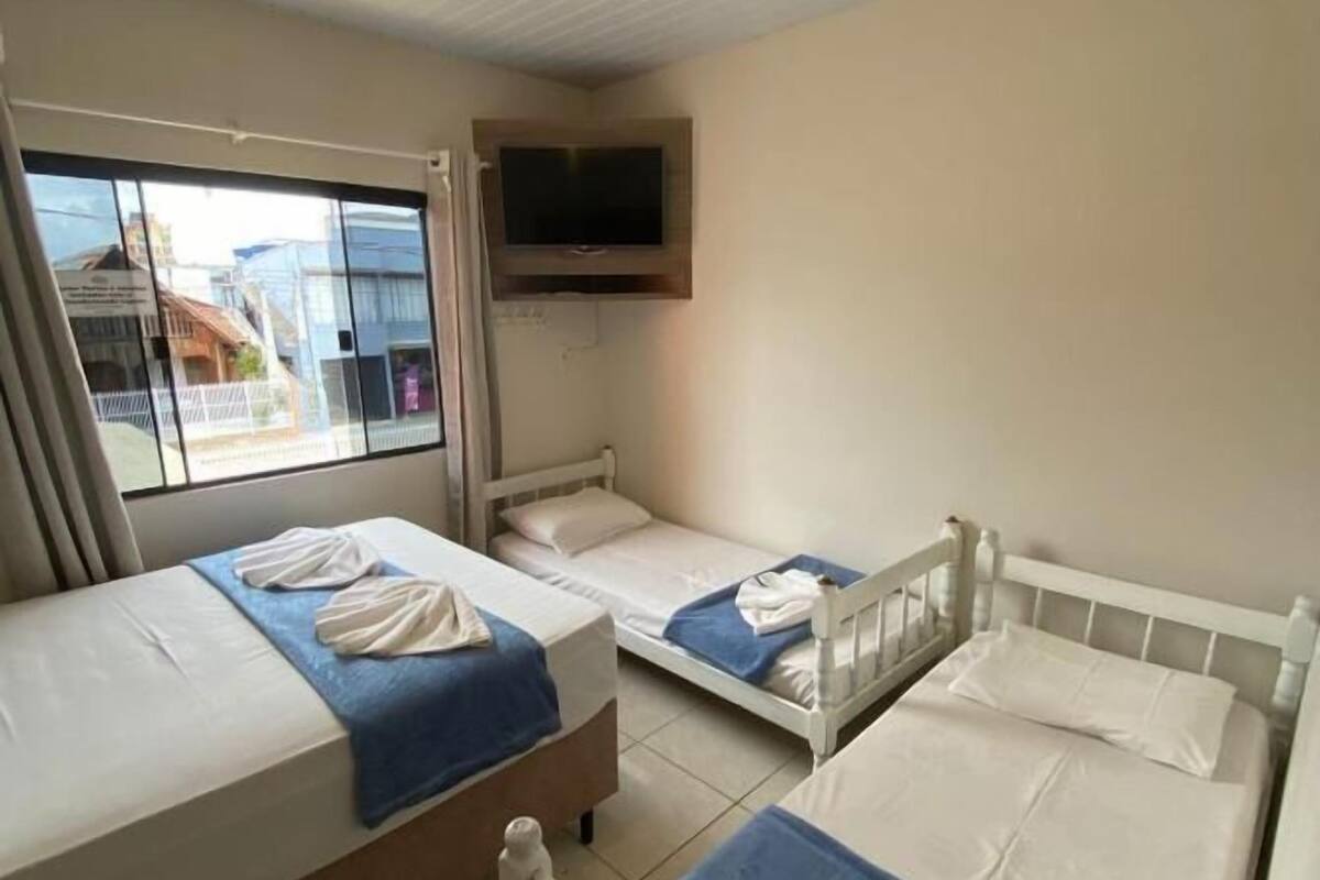 Ein Zimmer mit drei Einzelbetten, jedes mit einer blauen Decke und weißen Handtüchern. An der Wand über den Betten ist ein Flachbildfernseher angebracht.