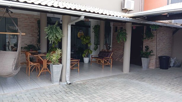 A covered outdoor seating area with a table and chairs, potted plants, and a hanging chair. - Pousada Cantinho da Jake (Penha)