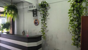 Een receptie met een balie, een hangplant, een bord aan de muur en een plant in pot.