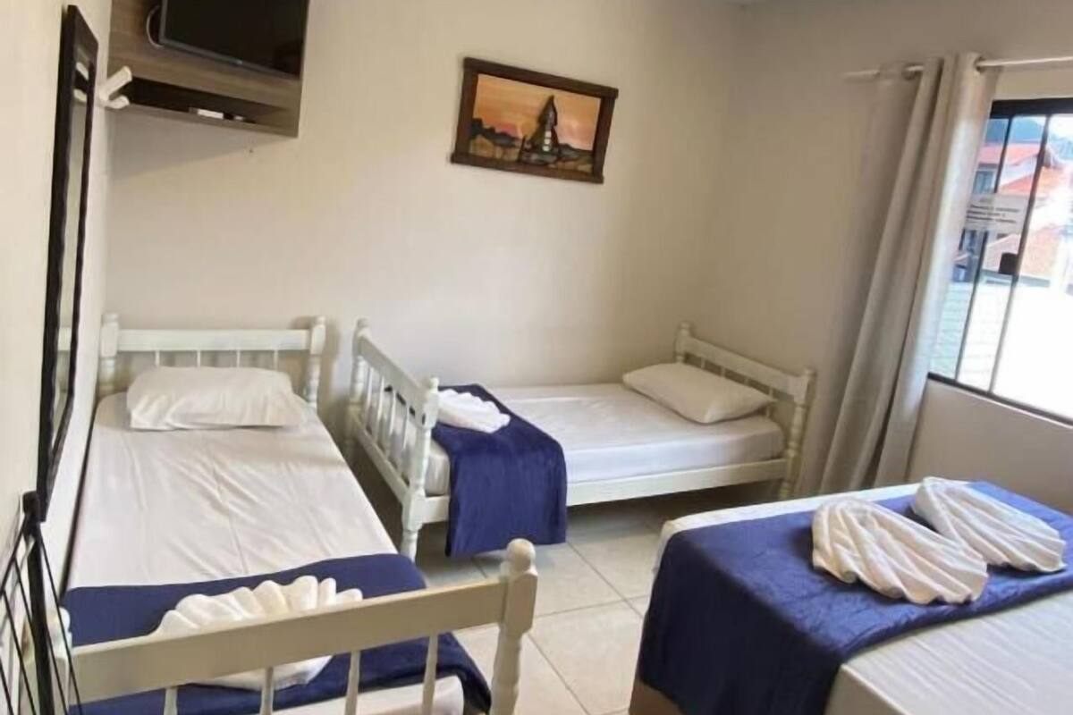 Ein Zimmer mit drei Einzelbetten, einem an der Wand montierten Fernseher und einem Gemälde über den Betten.